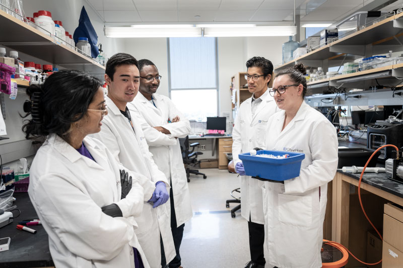 Five researchers in lab coats talking together in a laboratory.
